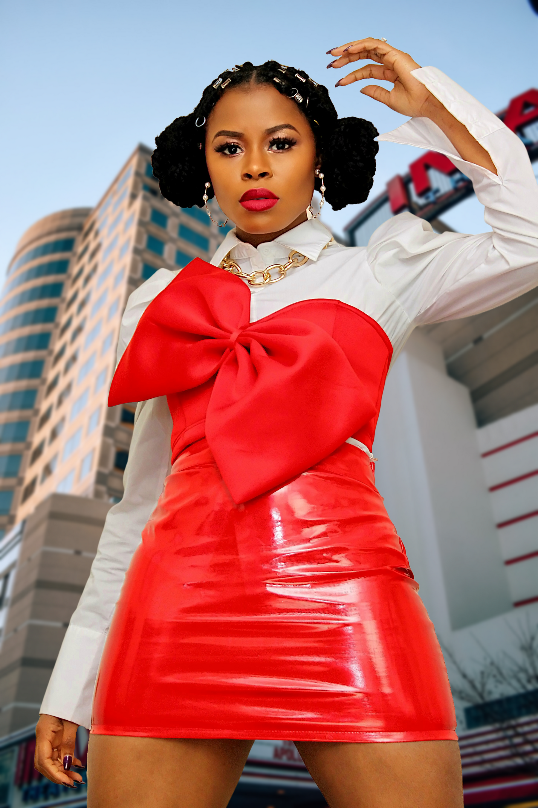 A female wearing a white shirt and red crop oversized bowtie top with shinning red leather skirt. 